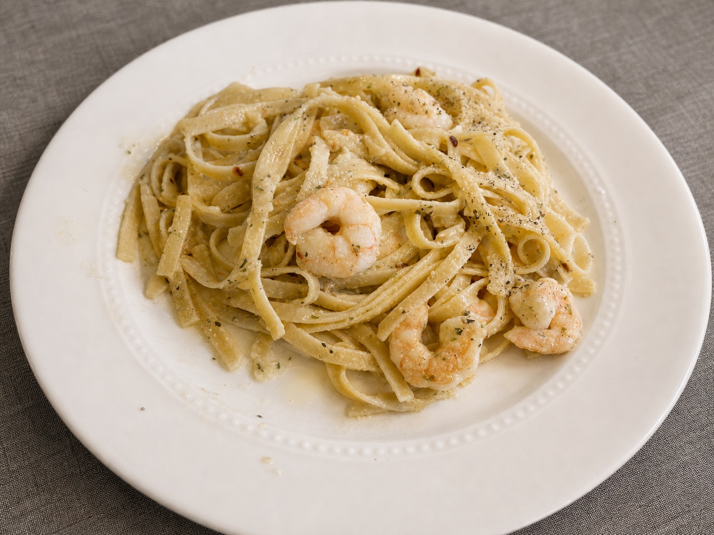 Close-up of garlic butter shrimp fettuccine with Parmesan, herbs, red pepper flakes, and black pepper on a white plate