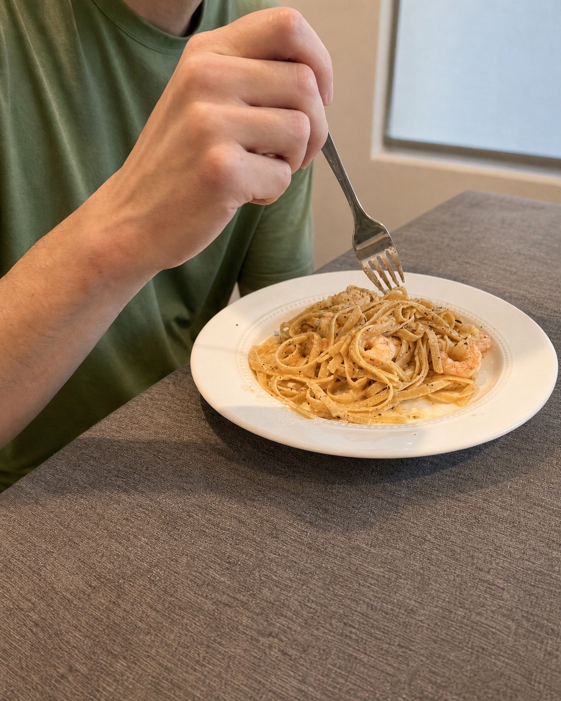 A person in a green shirt lifting garlic butter shrimp pasta from a white plate with a fork